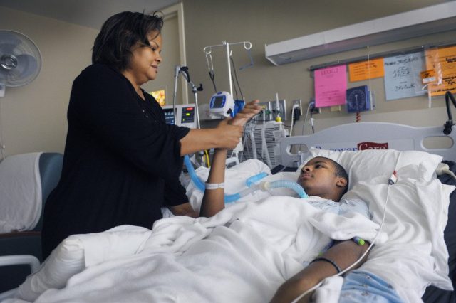 Zondra Magness works on moving her son's arm in his hospital room. Monroe Bird III "Trey" is at the Kaiser Rehabilitation Center in Tulsa, OK. Tuesday May 12, 2015. Bird was shot and paralyzed by a security guard in the parking lot of the Deerfield Estates Apartments when Bird was spotted in the car with a girl earlier this year. Photo by Brandi Simons for The Frontier.